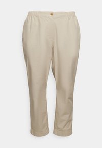 Pantalons en coton beige avec une taille élastique, dotés d'une fermeture à bouton à l'avant et de poches latérales, s'effilant légèrement vers les poignets.