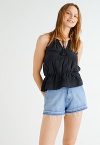 Juoda smockinė peplum palaidinė su kaklo surišimu, derinama su šviesiai mėlynomis džinsinėmis šortais, turinčiais ištrintus kraštus.