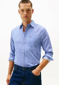 Blå og hvid stribet skjorte med krave, enkelt brystlomme og oprullede ærmer, parret med mørke denimjeans.