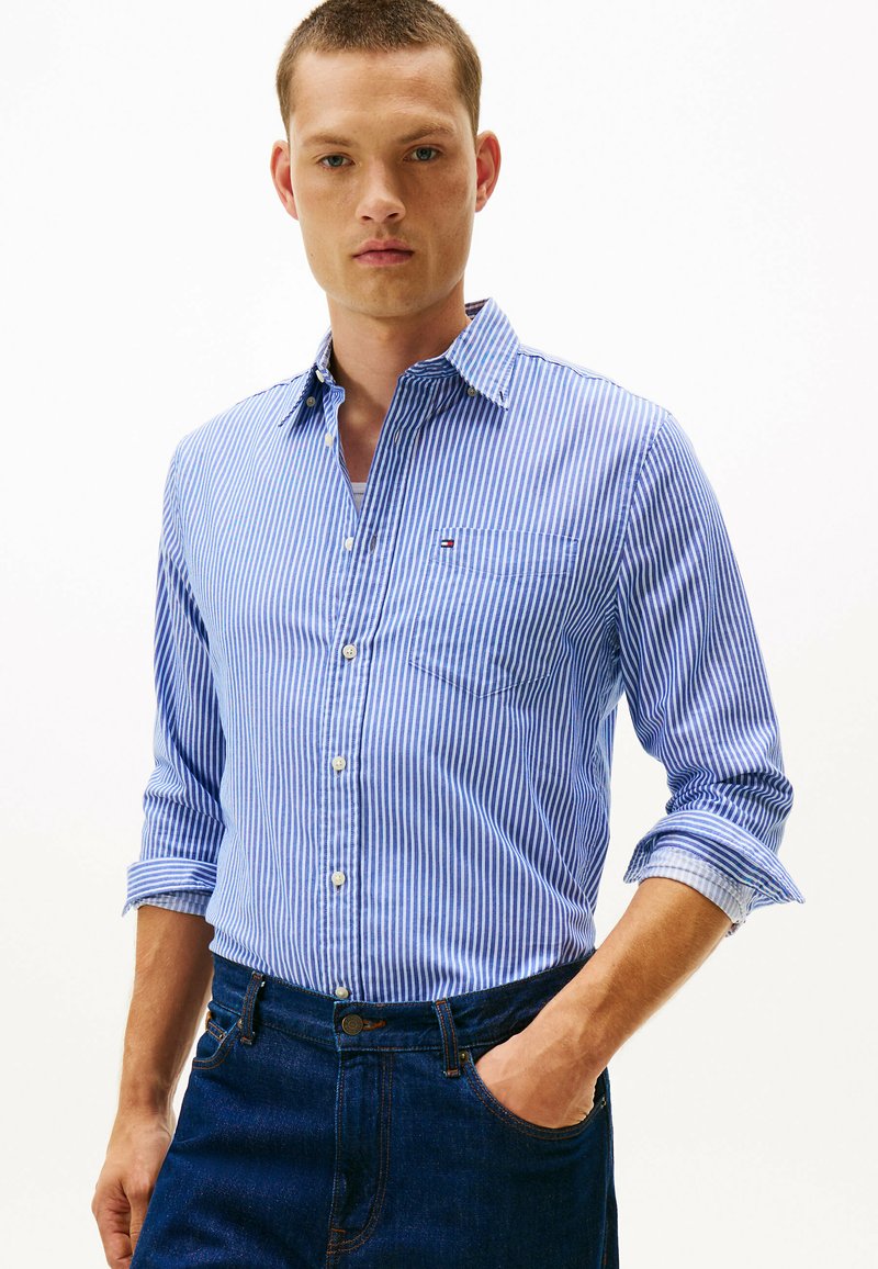 Blå og hvid stribet skjorte med krave, enkelt brystlomme og oprullede ærmer, parret med mørke denimjeans.