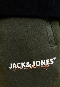 Olivenfarvede joggers med ribbet talje, sidelomme og trykt "JACK & JONES" logo i hvidt med et kursiv accent.