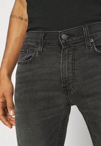 Svarta jeans i denim med smal passform, fem-fickorsdesign, knappstängning och diskret sömdekoration längs sömmarna.