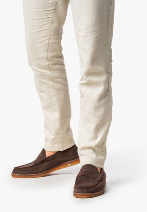 Dark brown suede loafers with a textured upper, featuring a low-profile design and a contrasting light brown sole. Smooth finish, no visible hardware.