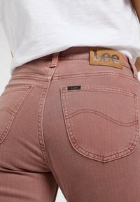 Jeans Lee en suave denim rosa, con un parche de cuero en la parte trasera con el logo y detalle de costura en los bolsillos traseros curvados.