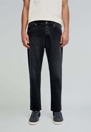 Zwarte denim jeans met een rechte pasvorm, vijf zakken en subtiele stiksels, gecombineerd met grijze sneakers. Eenvoudig, casual ontwerp.