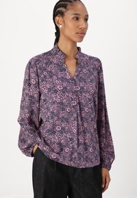 Blusa floreale in rosa e blu navy con colletto alla cinese, maniche lunghe a palloncino e patta con bottoni. Presenta un piccolo motivo floreale e una texture liscia.