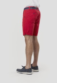 Rdeče bombažne kratke hlače z zavihanim robom, opremljene z modro-belim črtastim pasom. Oblečene z temno modrimi čevlji, ki prikazujejo ležerno zasnovo.