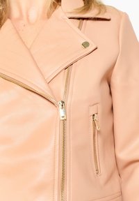 Chaqueta de moto de imitación cuero en rosa claro con detalles acolchados diagonales, cremalleras doradas y cuello con muesca.