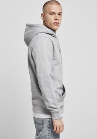 Grå hættebluse med kengurulomme, snoretræk i hætten og ribbede manchetter. Båret over en hvid skjorte, parret med lyse denimjeans.