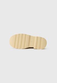 Suola di scarpa beige chiaro con grip testurizzato, caratterizzata da righe orizzontali e un'area centrale liscia. Design semplice con dettagli minimi.