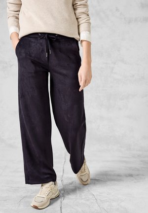 Breda ben, mörk marinblå byxor i mjukt, texturerat tyg med dragsko i midjan, kombinerat med ljusa sneakers.