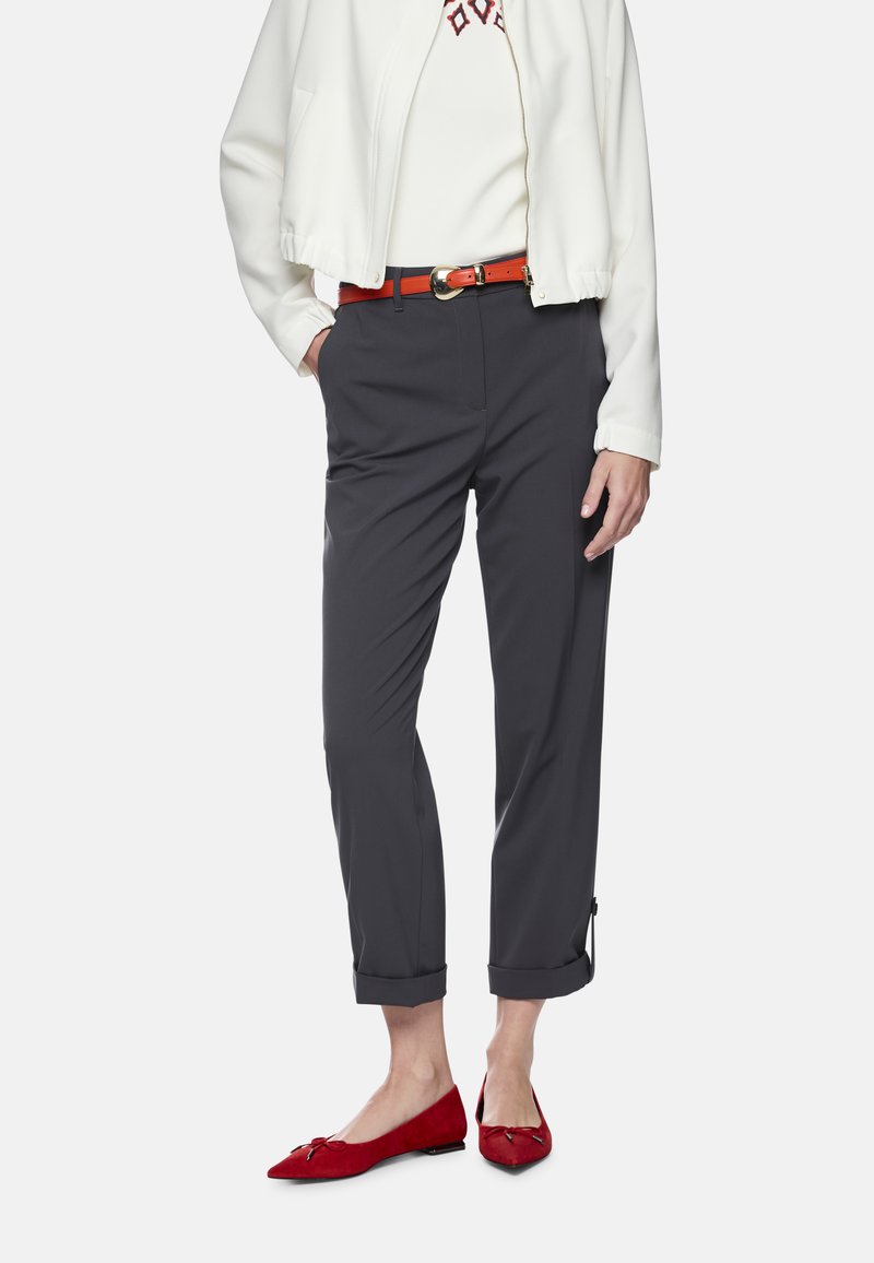 Graue, maßgeschneiderte Hosen mit hochgekrempelten Säumen, kombiniert mit einer weißen Bomberjacke. Ergänzt durch einen roten Gürtel und rote, mit einer Schleife verzierte Ballerinas.