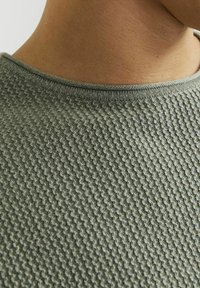 Groene gebreide trui met een textuurpatroon, geribbelde ronde hals en een gladde afwerking, met de nadruk op het ingewikkelde ontwerp van de stof.