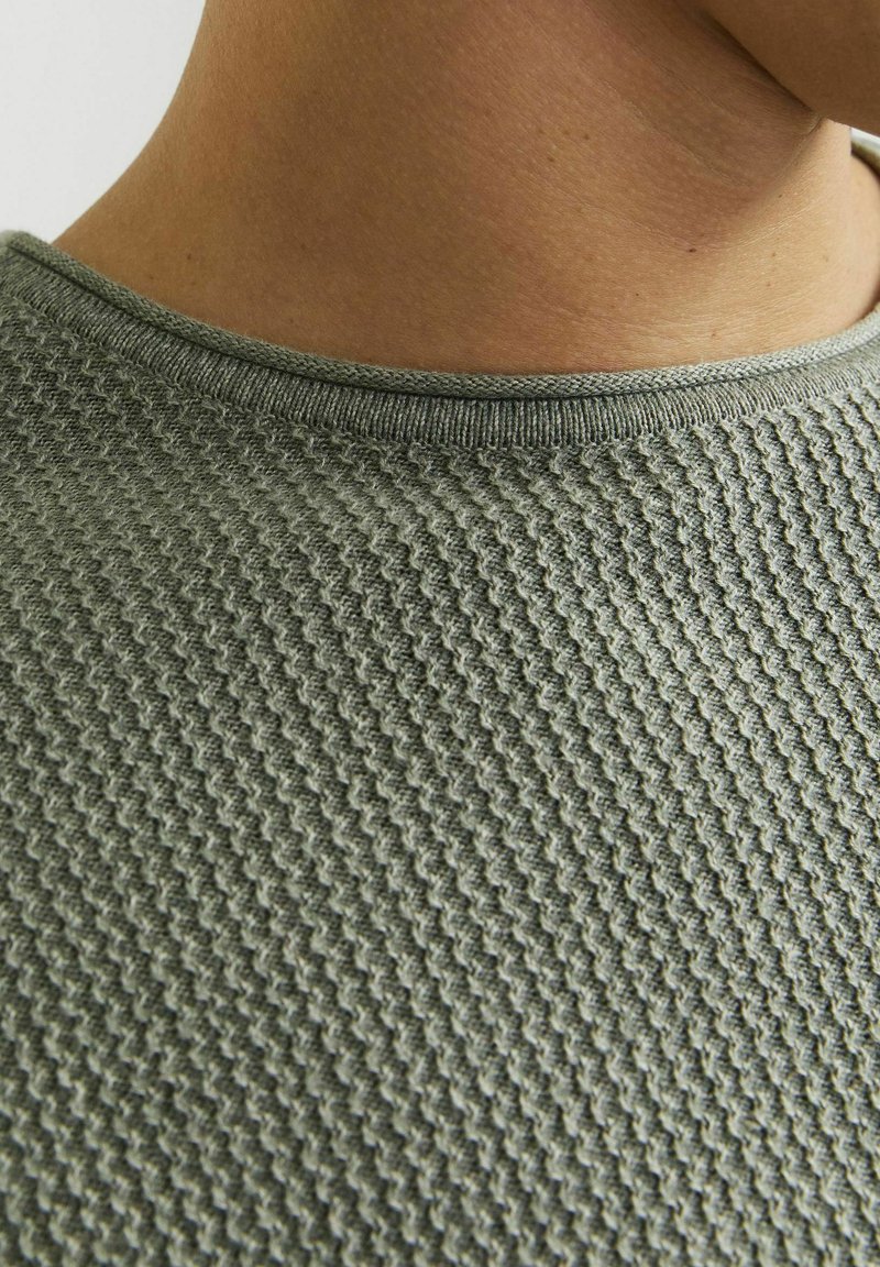 Groene gebreide trui met een textuurpatroon, geribbelde ronde hals en een gladde afwerking, met de nadruk op het ingewikkelde ontwerp van de stof.