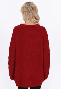 Roter gestrickter Pullover mit weitem Schnitt, der gestickte Blumenmuster an den Ärmeln und einen runden Ausschnitt aufweist. Weicher Stoff.