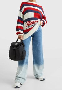 Gestrickter Pullover mit roten, weißen und marineblauen Streifen, mit dem Schriftzug "Tommy Jeans". Hellblaue Jeans mit weitem Bein und schwarzer Rucksack mit Klappverschluss.