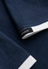 Námořnická modrá bavlněná tričko s bílými manžetami, šitým lemem a černou etiketou s textem "ombre" poblíž manžety. Hladká textura.