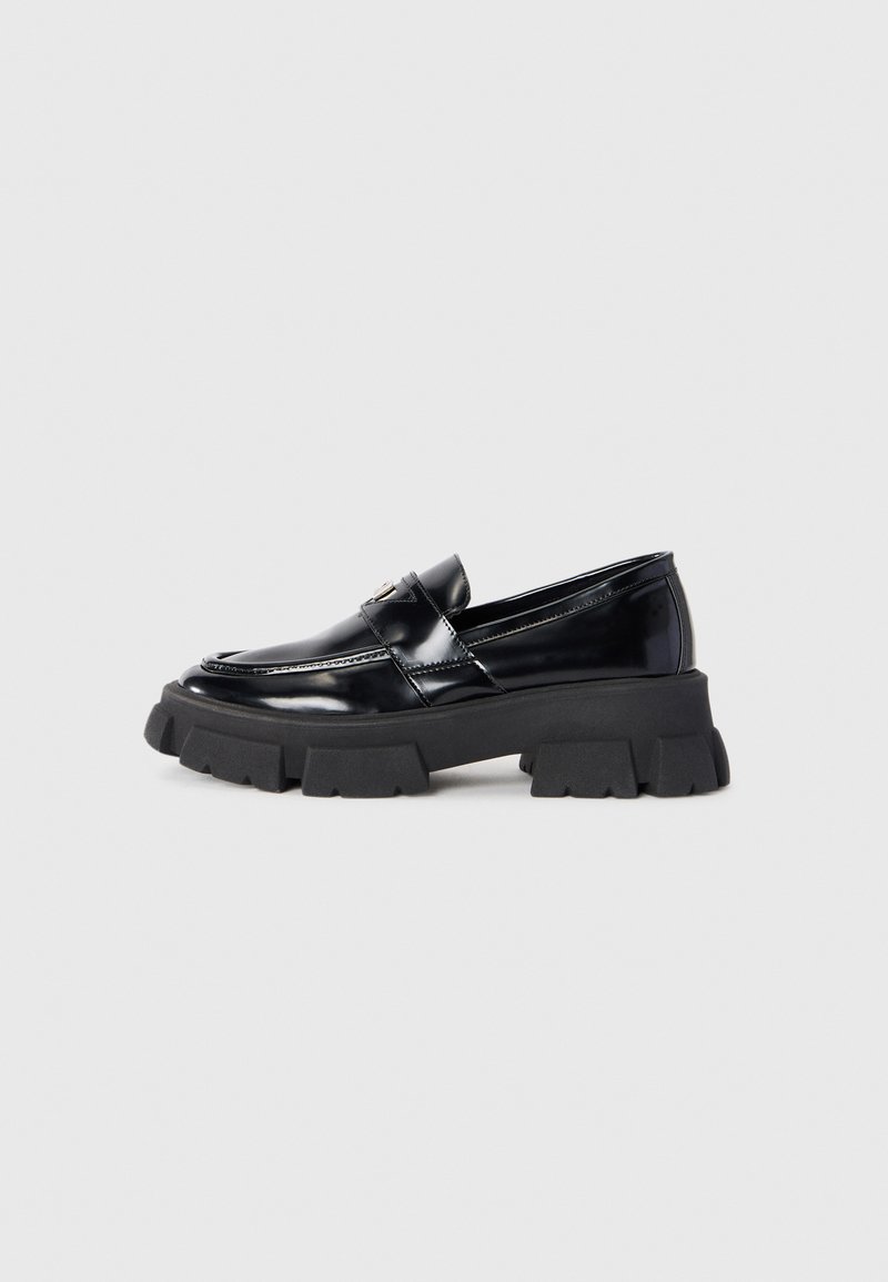 Mocassins en cuir verni noir avec une semelle plate-forme imposante noire. Les caractéristiques comprennent un bout arrondi et des coutures décoratives sur le devant.