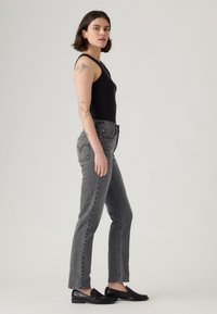 Črn rebrast bodysuit, sivi jeans z visokim pasom in ravnim krojem, z rahlim dubljenjem, klasičen pet žepni dizajn in črne loafer čevlje.