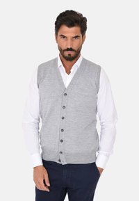 Gilet grigio lavorato a maglia con scollo a V, caratterizzato da sei bottoni scuri e orlo a coste, indossato sopra una camicia bianca con bottoni. Texture liscia.