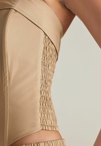 Beige bandeau-top med sidofållningar, slät textur och elegant design, med elastiska detaljer för extra stretch.