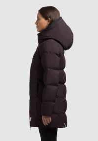 Chaqueta acolchada de color púrpura oscuro con capucha, diseño acolchado y cremallera lateral. La tela se ve suave con un ligero brillo.