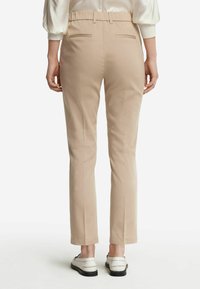 Beige skräddarsydda byxor med en åtsittande midja, två bakfickor och rakt bendesign, i kombination med vita slip-on skor.