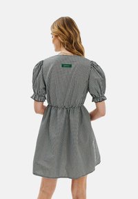 Šaty z čiernobieleho károvaného materiálu s nadýchanými rukávmi, elastickým pásom a zelenou štítkom značky na zadnej strane. Mäkka textília s voľným siluetou.