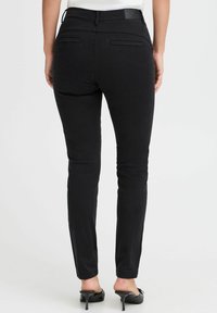 Melni, šauri džinsi ar vidēju jostasvietu, kuriem ir divas aizmugurējās kabatas un gluda, elastīga auduma. Minimālisma dizains ar smalkām diegu šuvēm.