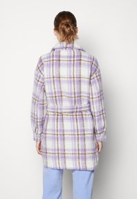 Manteau à carreaux en lavande, blanc et marron avec une ceinture. Présente un col et des manches longues. Tissu doux et texturé avec une coupe ample.