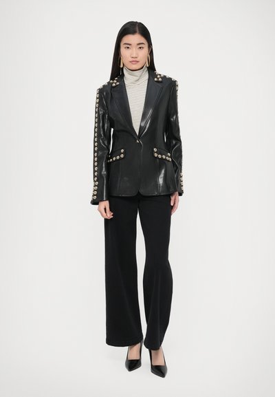 Fekete bőr blézer arany színű gombokkal a vállakon és a zsebeknél, szürke-fehér csíkos garbóval párosítva.