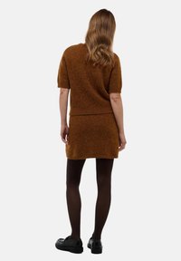Ensemble en tricot marron composé d'un pull et d'une jupe, à manches courtes, avec une texture douce et un design ajusté, associé à des collants foncés et des chaussures noires.