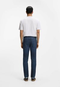 Miesten tummansiniset suoralahkeiset farkut yhdistettynä valkoiseen lyhythihaiseen t-paitaan ja mustiin kenkiin, kuvattu takaa.