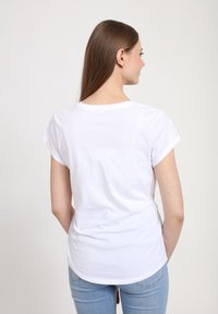 Camiseta de algodón blanca con mangas cortas enrolladas, cuello redondo y un corte relajado. La parte trasera es lisa, sin patrones ni embellishments.