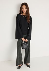 Must pikkade varrukatega pluus paksud õlgadega; triibulised laiade säärtega püksid; must käekott hõbedaste naeltega; mustad teravate nina jaotatud kingad.