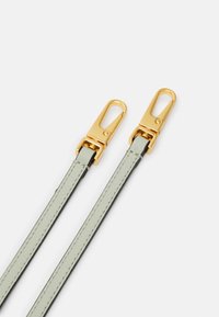 Kaksi vaaleanvihreää nahkaista hihnaa, joissa on kultasävytteiset metalliklipsit. Ominaisuuksina on kontrastivärinen ommel ja sileä pinta. Sopii erilaisiin lisävarusteisiin.