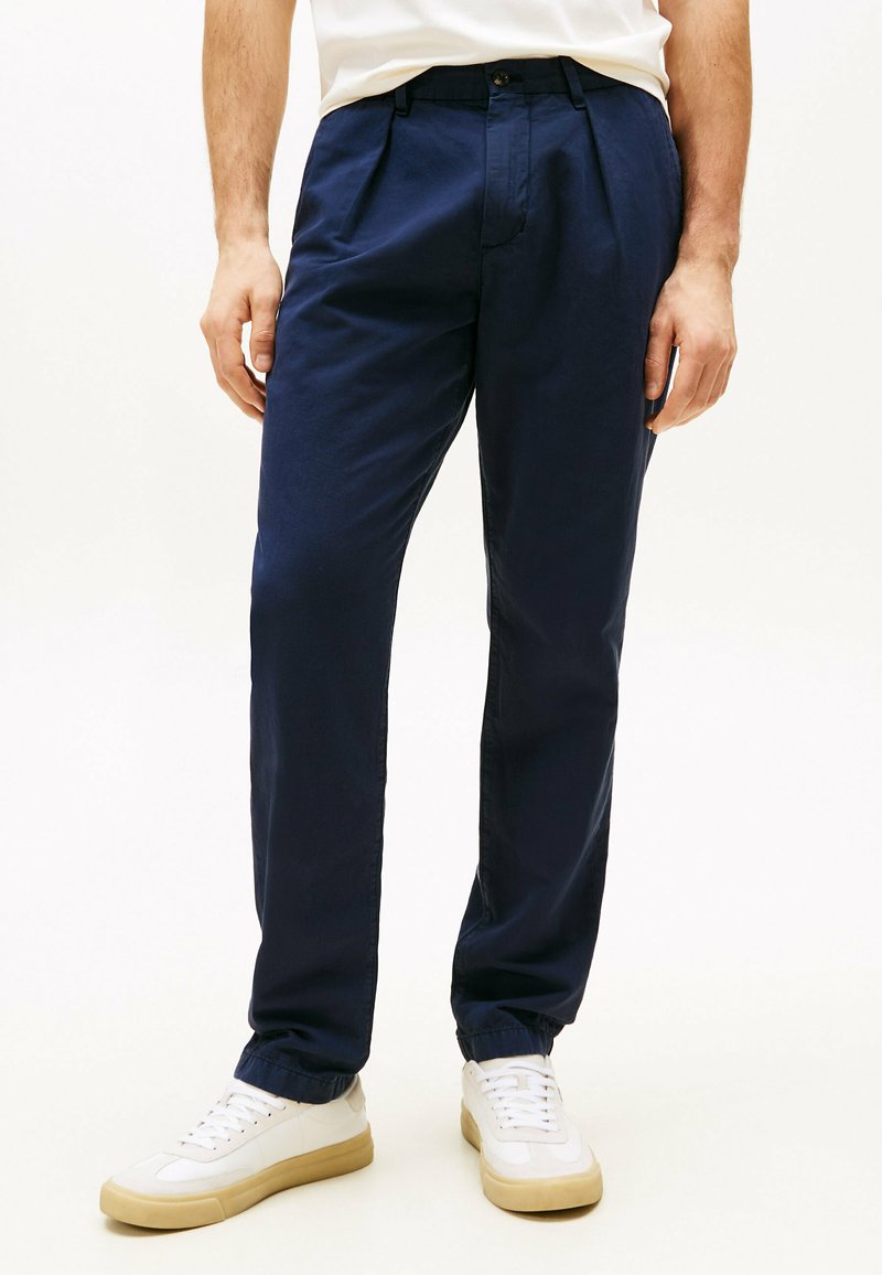 Pantaloni blu navy in cotone, con vestibilità comoda, frontale plissettato e polsini elasticizzati, abbinati a sneakers bianche.