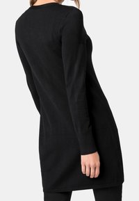 Svart stickad långärmad tunika med rundad halsringning. Enhetlig textur och avslappnad passform, som sträcker sig till mitten av låret, med ribbade manschettdetaljer.