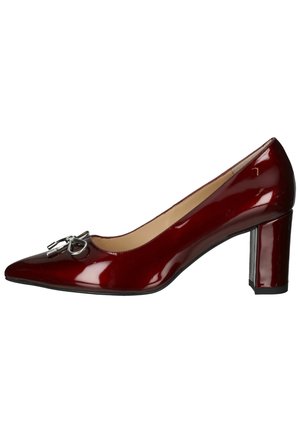 Czerwony lakierowany but na wysokim obcasie z ostrym noskiem i średniej wysokości słupkiem, zdobiony srebrnym akcentem dekoracyjnym.