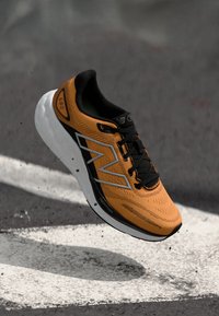 Oranje en zwarte sport sneaker met een bovenwerk van mesh, voorzien van een vetgedrukte witte logo, textuuraccenten en een gevoerde witte zool.