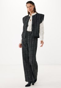 Černobílá vesta z tkaniny s krátkými rukávy, spárovaná s odpovídajícími kalhotami širokého střihu; obě kusy mají kostkovaný vzor a texturovaný povrch.