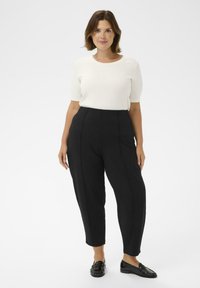 Pulover alb cu mânecă scurtă și pantaloni negri cu talie înaltă și pliuri, asortați cu mocasini negri; finisaje din material neted.