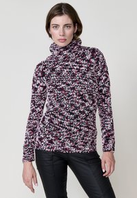 Pull en tricot avec un col haut, dans un motif tacheté de rose, violet et noir ; texture douce, manches longues et coupe ajustée.