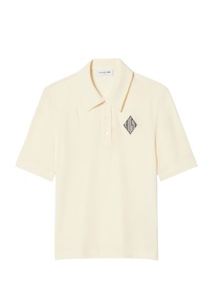 Polo de manga corta color crema con cuello, tapeta con tres botones y un logo "LACOSTE" en forma de diamante negro en el lado izquierdo del pecho.