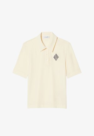 Polo de manga corta color crema con cuello, tapeta con tres botones y un logo "LACOSTE" en forma de diamante negro en el lado izquierdo del pecho.