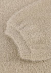 Beige, zachte stof met een fuzzy textuur en zichtbare vezels. Heeft een gebogen rand met een lichte plooi, wat de stofgewicht en val aangeeft.