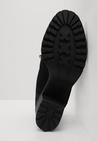 Zwarte enkellaars van suède met een geribbelde rubberen zool. Heeft een platte hak en een strak, minimalistisch ontwerp. Geen zichtbare logo's of versieringen.