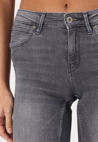 Jeans de mezclilla gris con un diseño ajustado, que cuentan con un cierre de botón, bolsillos delanteros y un ligero desgaste en la tela.