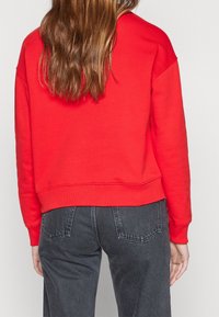 Rode sweatshirt met een ontspannen pasvorm en verlaagde schouders. Gemaakt van katoen, met een ribgebreide onderkant en manchetten. Draagt bij donkere denim jeans.