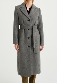 Cappotto con motivo pied de poule in bianco e nero, con vestibilità sartoriale, collo a risvolto, vita con cintura e chiusura con bottoni. Maniche lunghe e design fino al ginocchio.